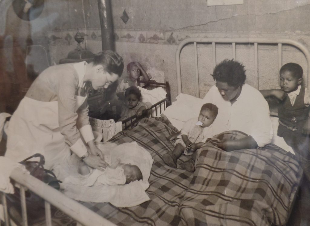 Image of Edna Schreiber treating her first patient surrounded by the patient's family