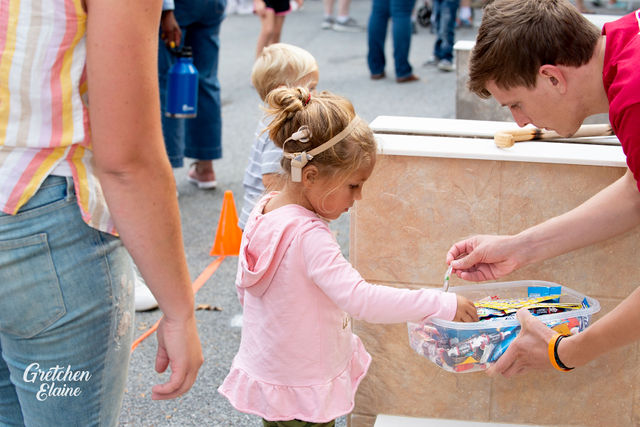Image of young girl with cochlear implant choosing a prize from a prize bin held by a young man volunteer 