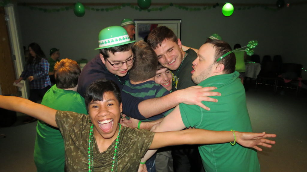 Group of teenagers and young adults enjoying our St. Patrick's Day dance party with a group hug and a celebratory photobomb