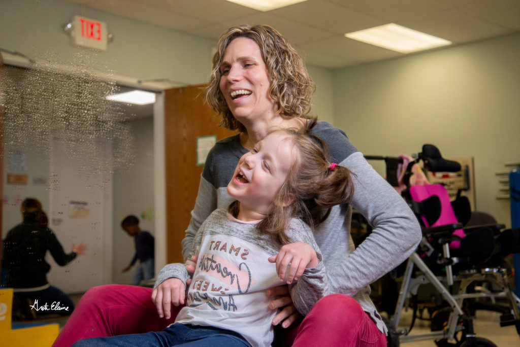 Physical therapist smiles while working with laughing young girl client on her physical therapy routine