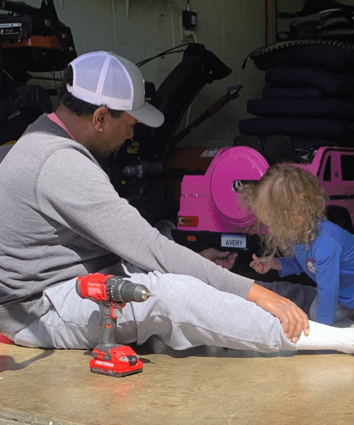 Avery and her dad working on a kid-sized pink jeep with the license plate that says "Avery".