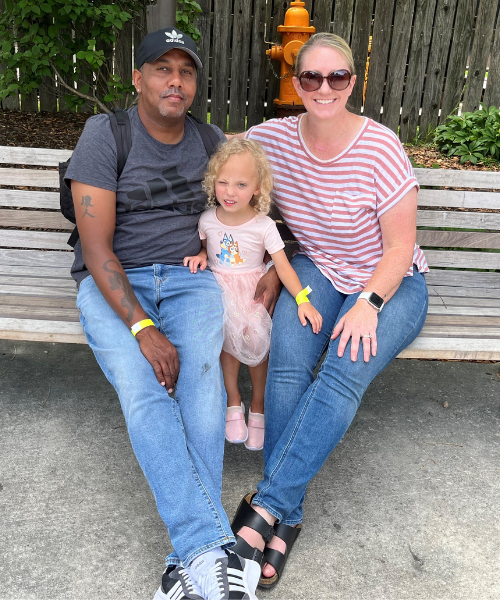 Avery and her mom and dad sitting on a wooden bench and smiling.