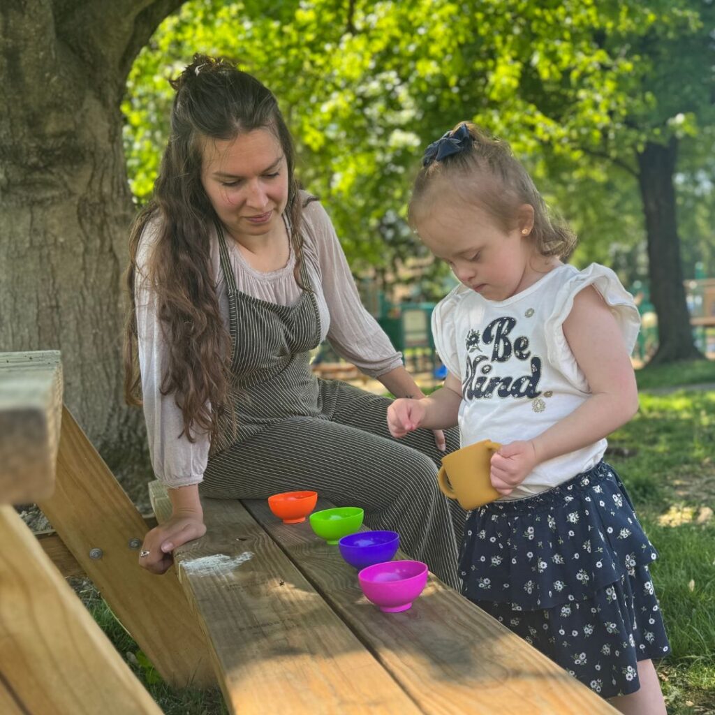 Young girl working on fine motor skills picking stones out of a mug and placing in colored bowls while occupational therapist supervises