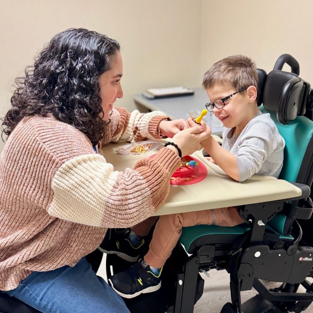 Young boy sitting in Rifton chair during speech therapy working on feeding