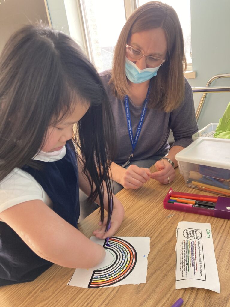Ellery coloring a rainbow picture with a therapist watching.