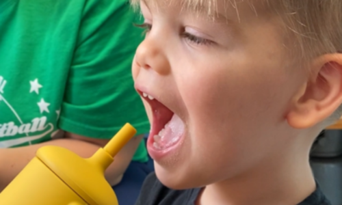 Finn with his mouth open trying out a yellow training cup.