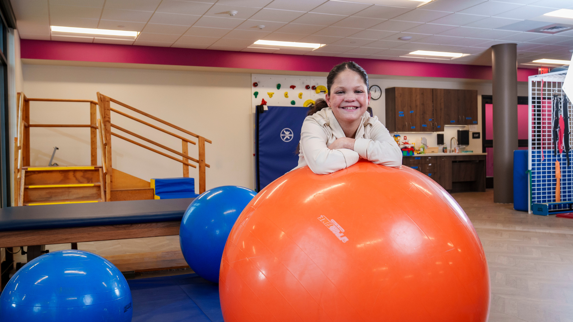girl facing camera lying on large orange ball in gym