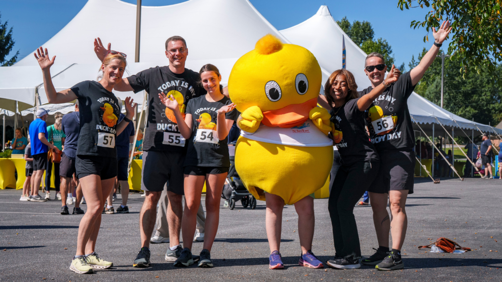 people posing with duckie race mascot at event