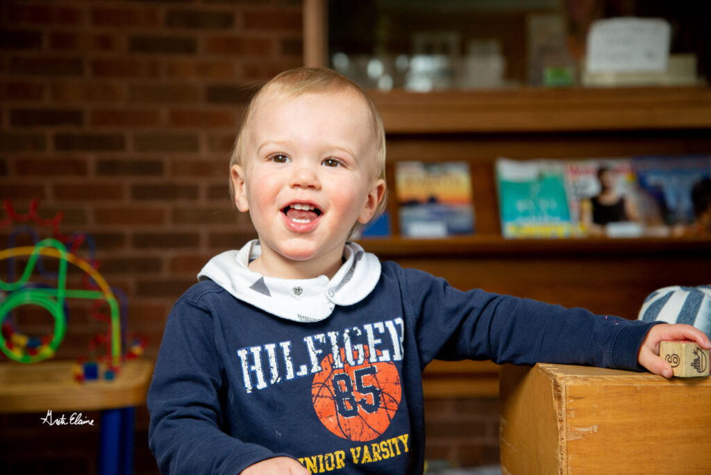 Toddler in blue smiling at the camera in classroom