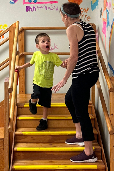 Brayden walking down stairs while physical therapist Libby assists.