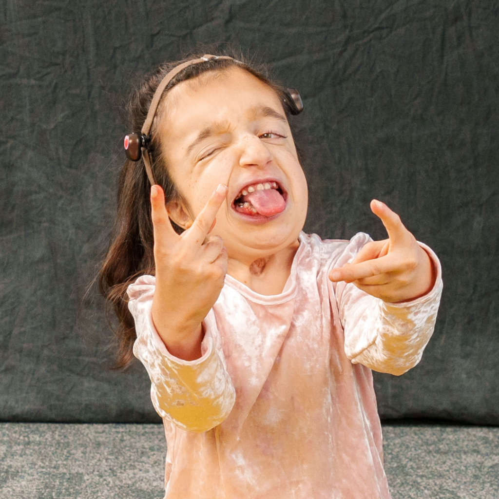little girl with tongue out and making peace signs with both her hands