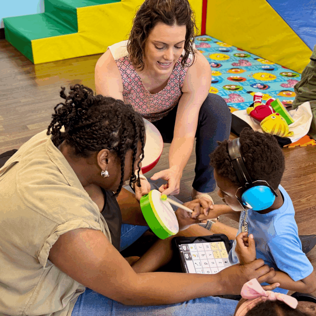 Little boy sitting with mom plays drums with instructor in music therapy camp