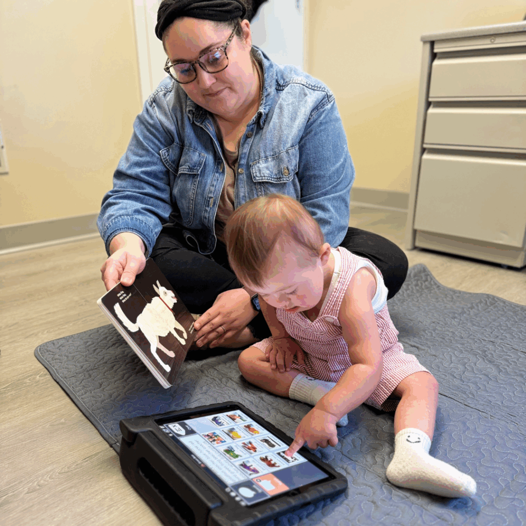 young boy using AAC device in speech therapy with therapist