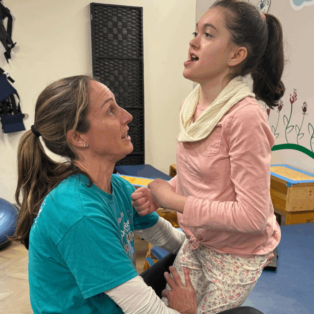 young girl practicing standing with the assistance of her female PT