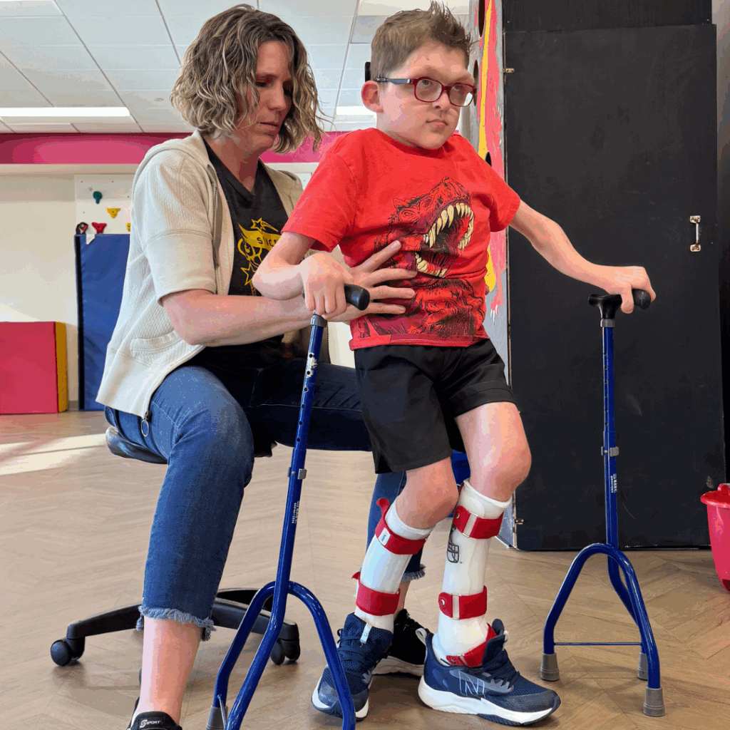 Young boy walking with canes assisted by female PT