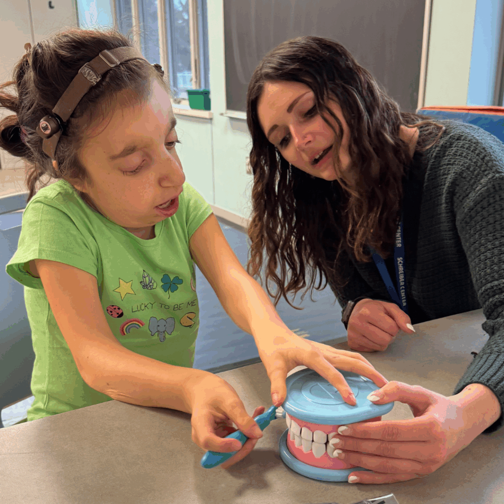 Young girl practicing brushing teeth on dental toys with female OT