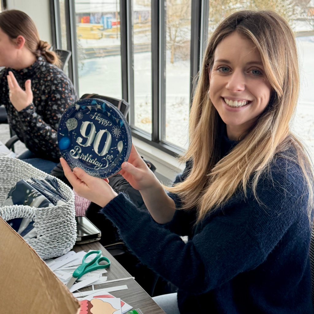 Volunteer woman holding up paper plate that reads "Happy 90th Birthday"