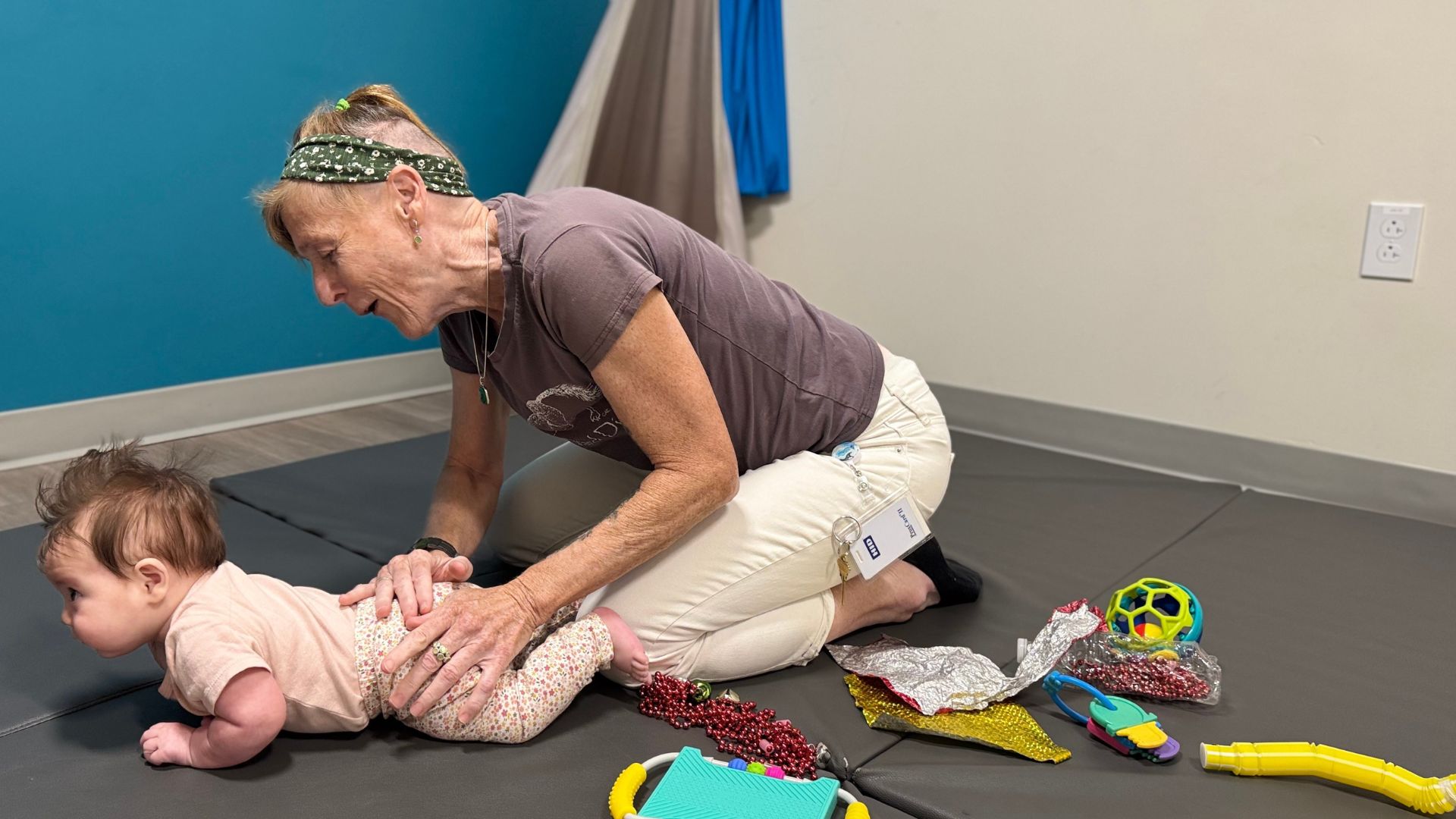 baby girl laying on stomach while female physical therapist kneels next to her