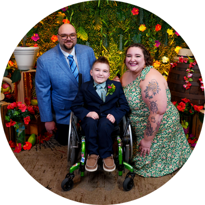 little boy in wheelchair flanked on either side by his kneeling parents