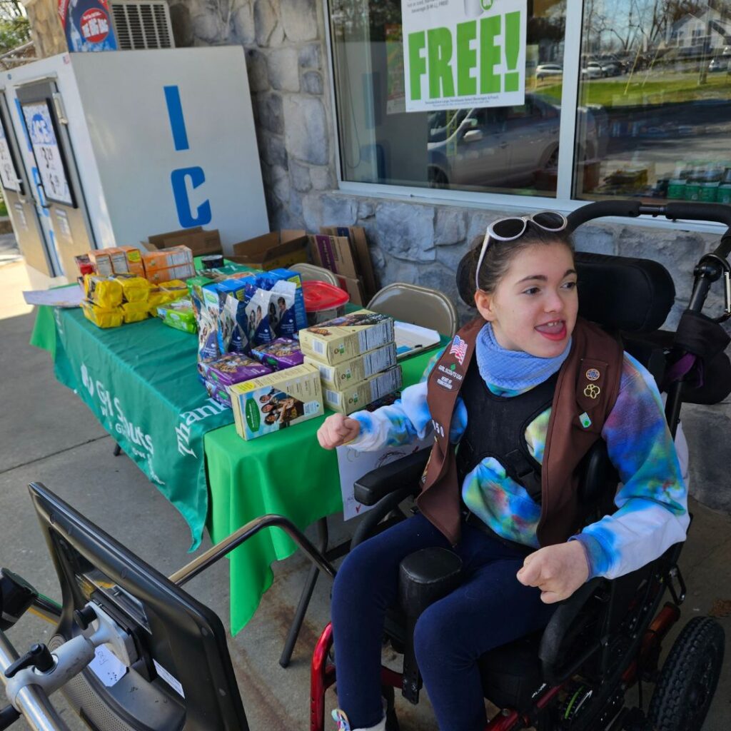 Girl scout in wheelchair with eye gaze device set up selling girl scout cookies