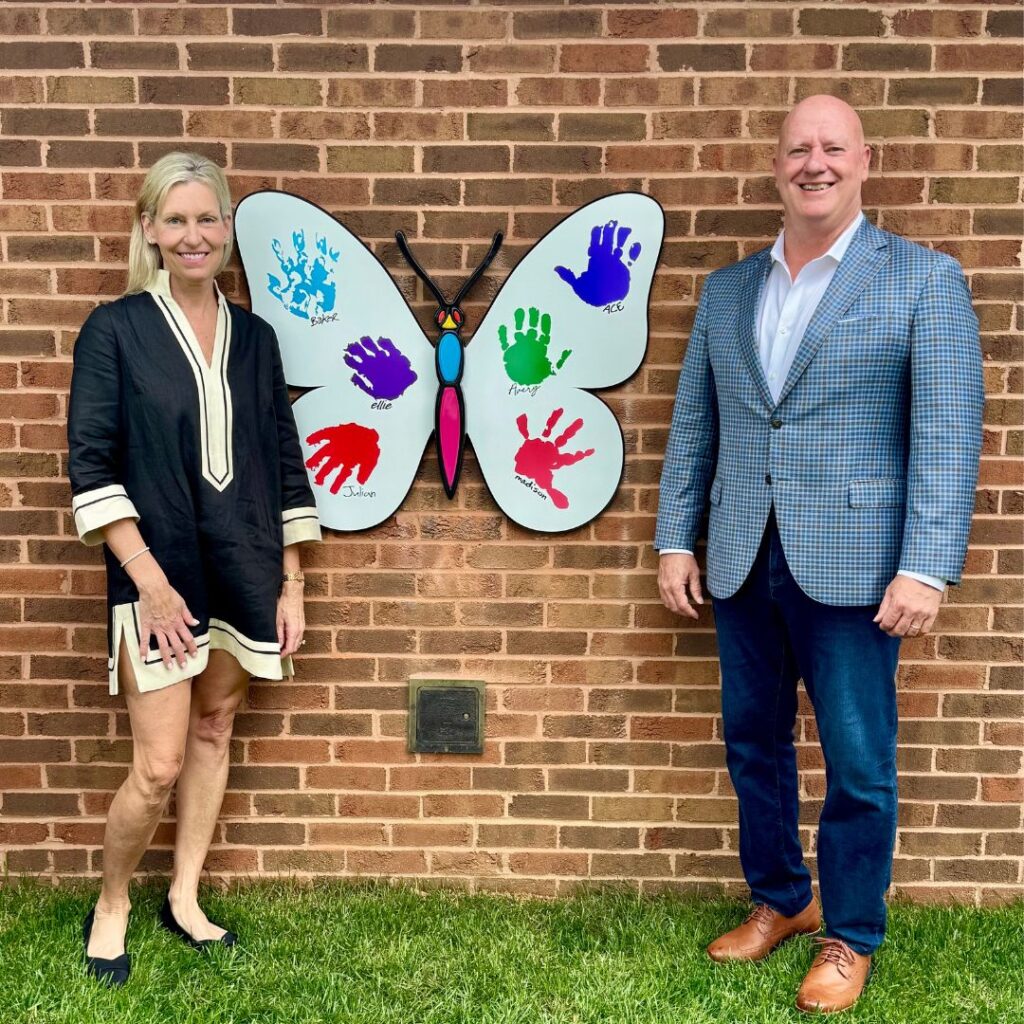 Woman and man standing next to butterfly art on a brick wall with toddler hand prints painted on it. 