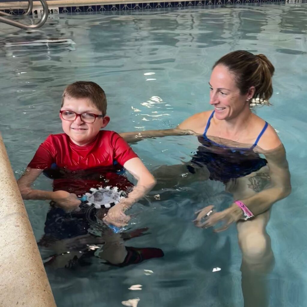 young boy in aquatic therapy with his physical therapist - both smiling
