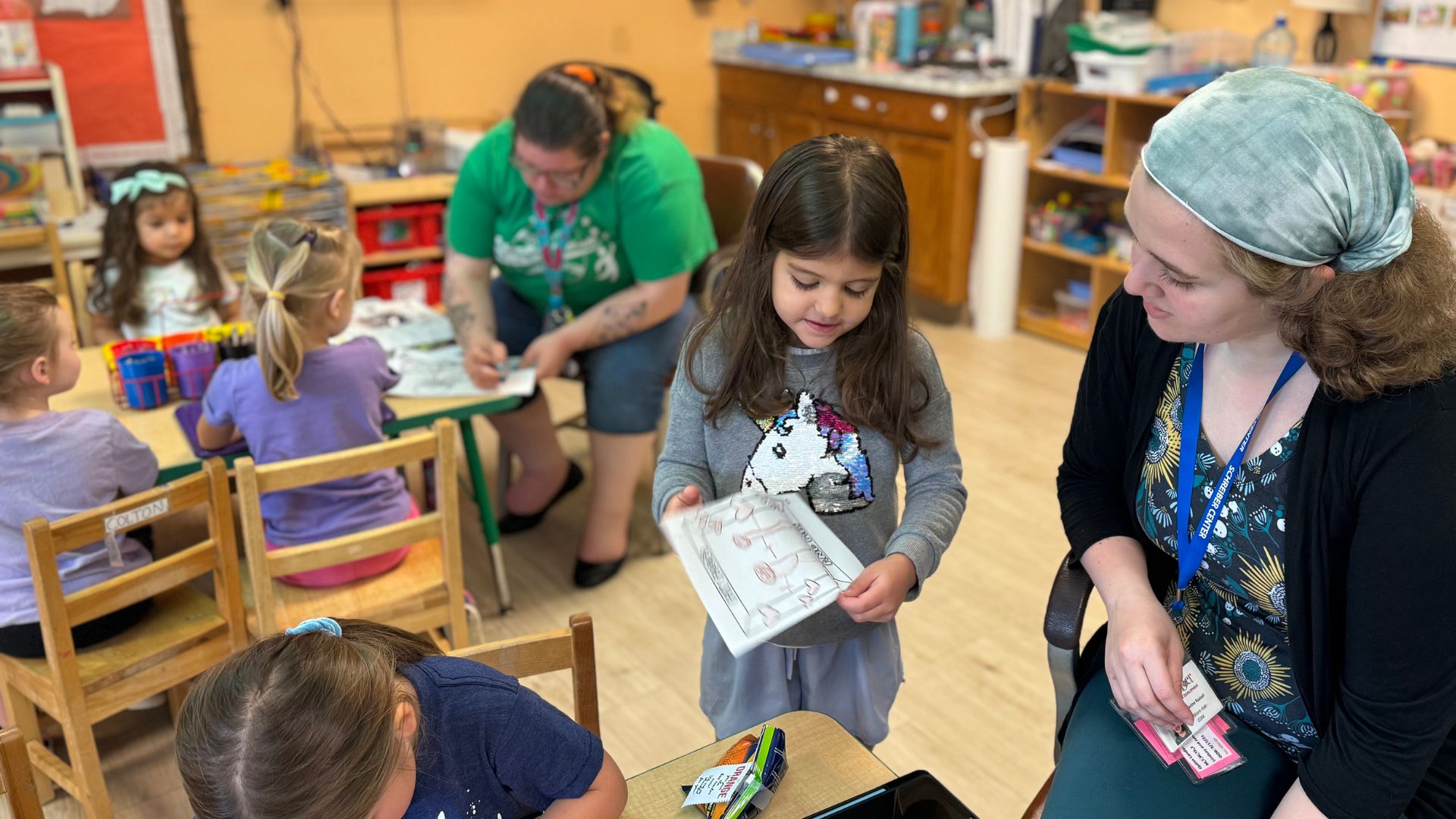Teacher looking over preschool students work in full classroom