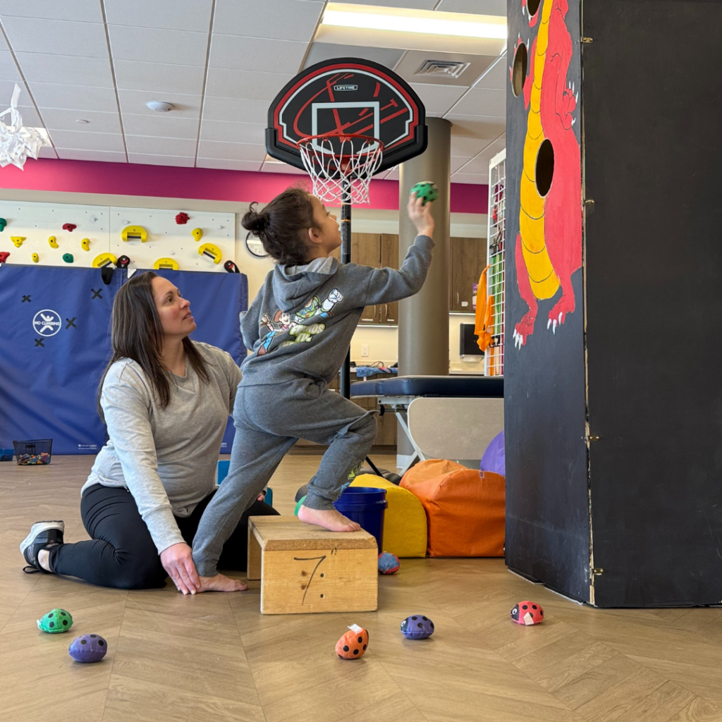 Child standing with one foot up on a 7 inch step while PT holds other foot flat on the ground to strengthen and stretch calf muscle