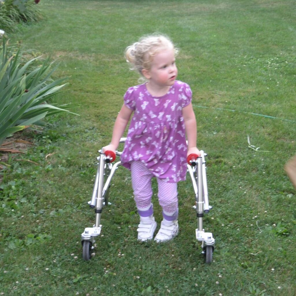 young girl standing in the grass with her reverse walker