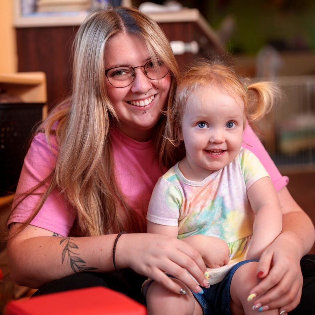 young girl sitting in her teachers lap both smiling at the camera
