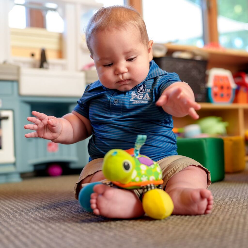 infant boy reaching for a stuffed turtle toy