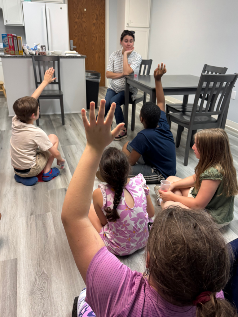 Kids sitting on the floor with their hands raised participating in group discussion