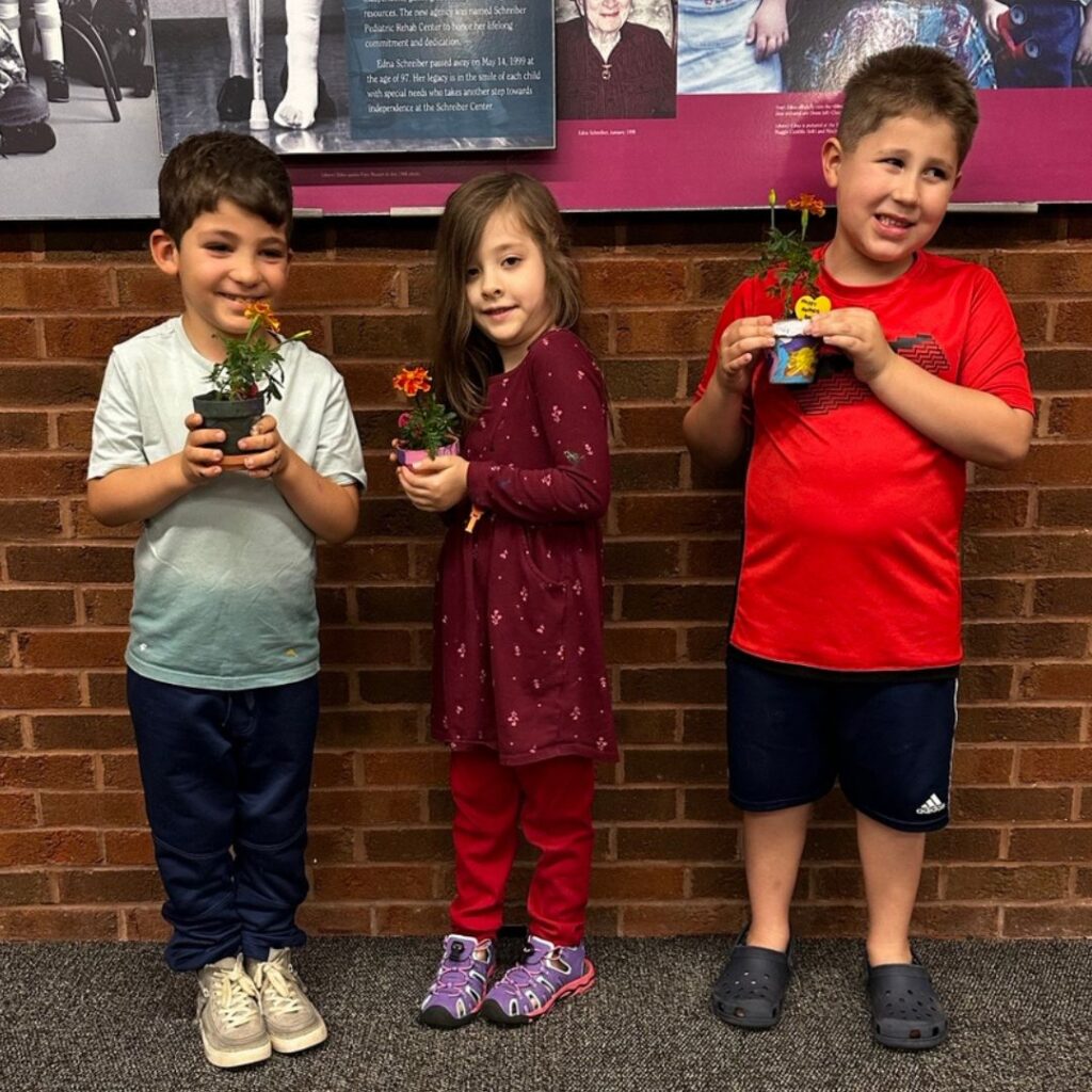 two boys and a girl standing in front of a brick wall holding the potted plants they made for mothers day