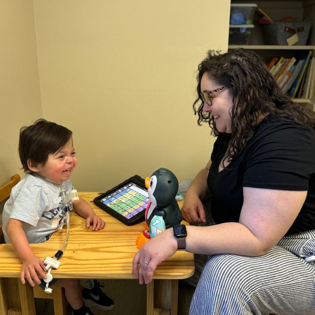 young boy using an aac device to communicate with his female therapist