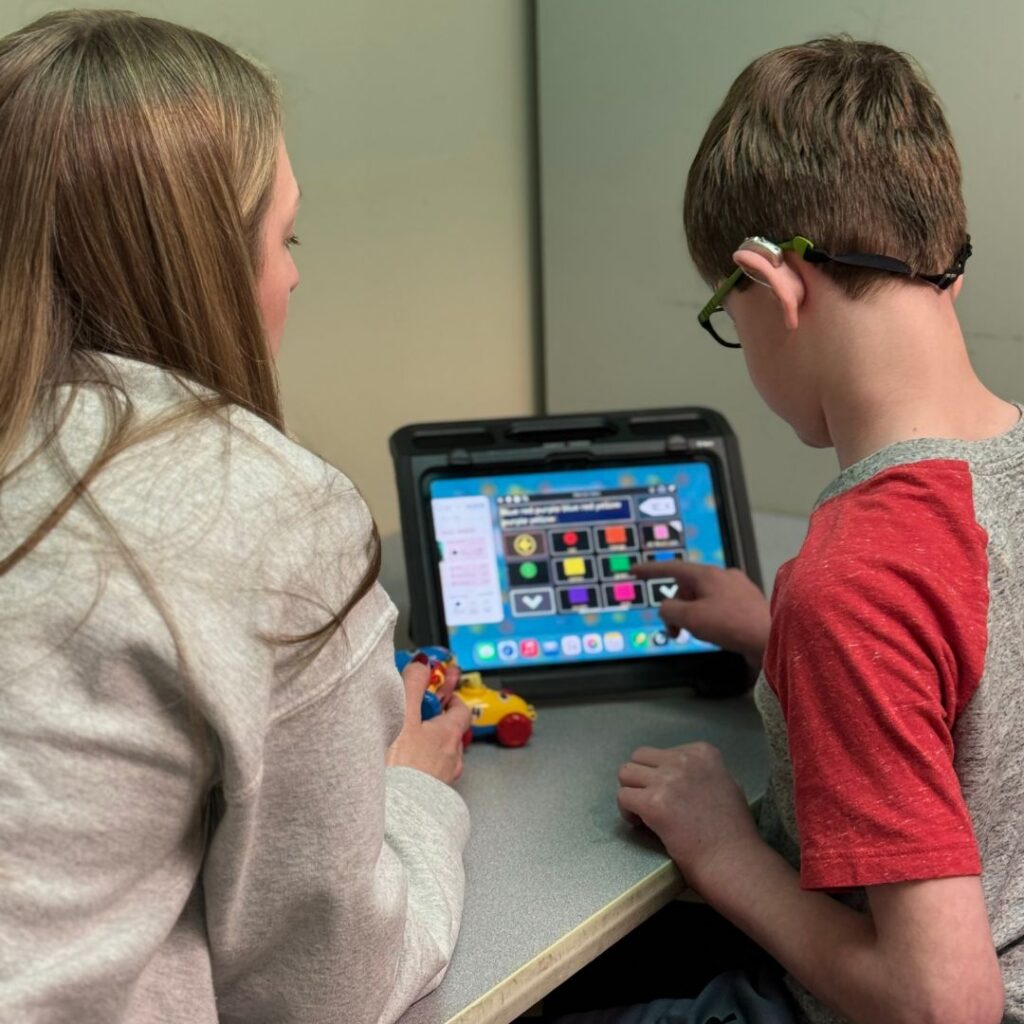 young boy using an aac device to communicate with his female therapist