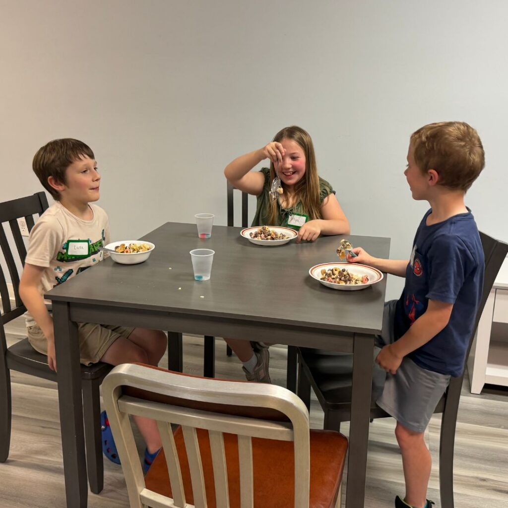 three kids sitting at a table enjoying a snack together