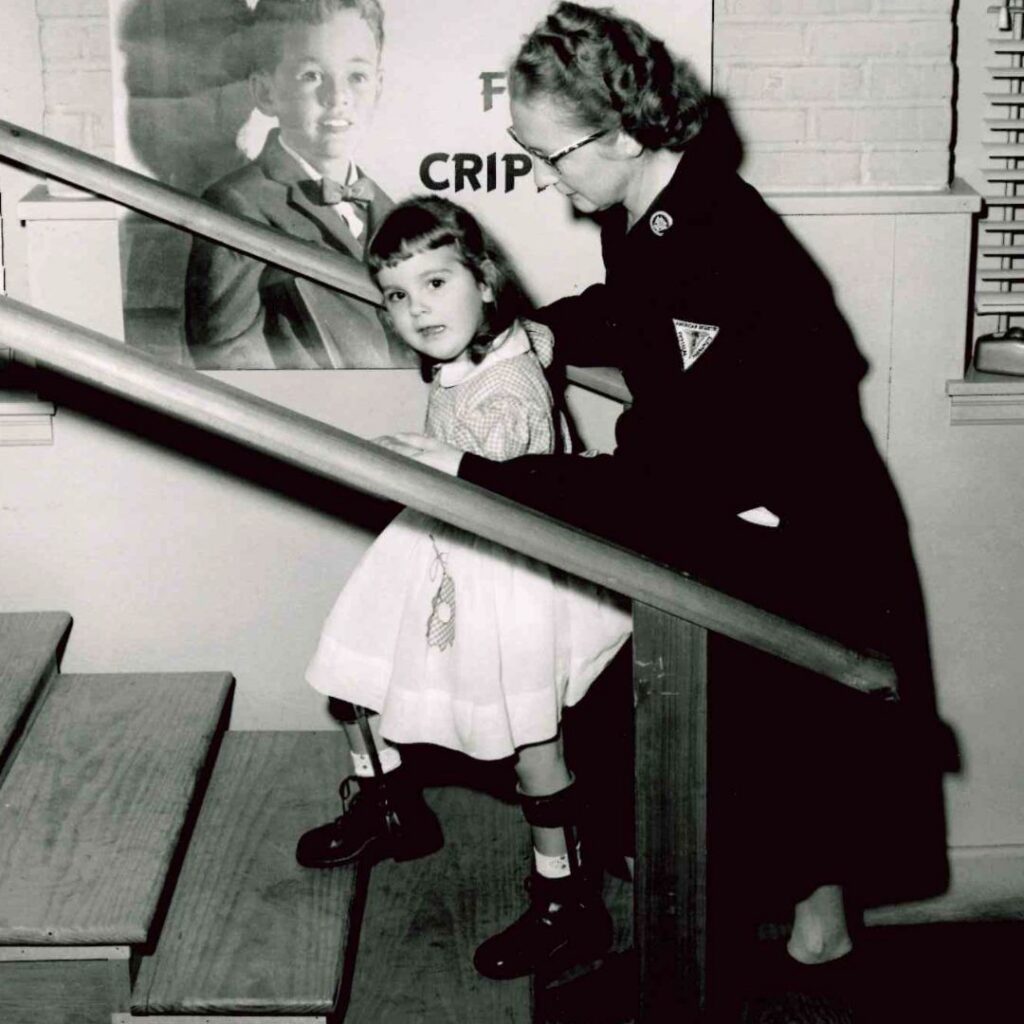 black and white photo of woman helping a little girl climb a set of stairs