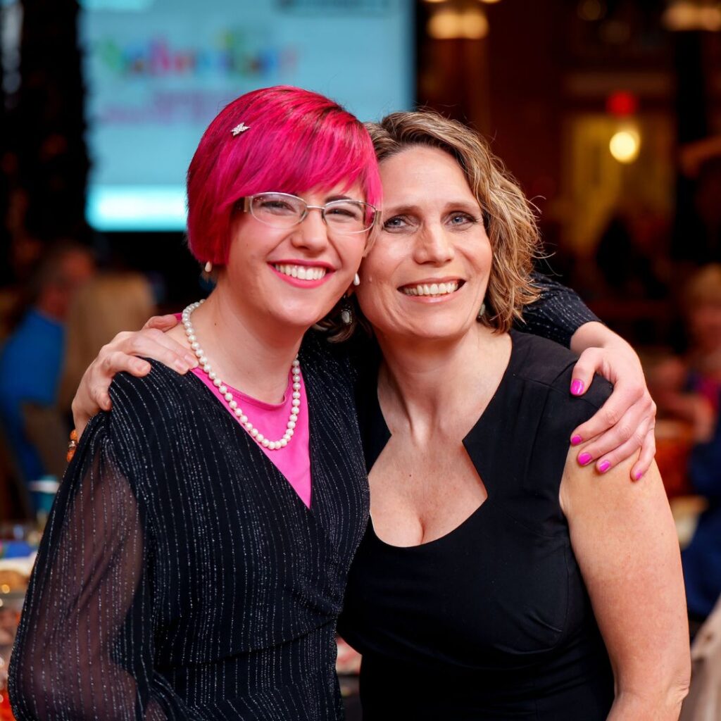 young woman with pink hair giving a side hug to her old PT at the Schreiber gala.